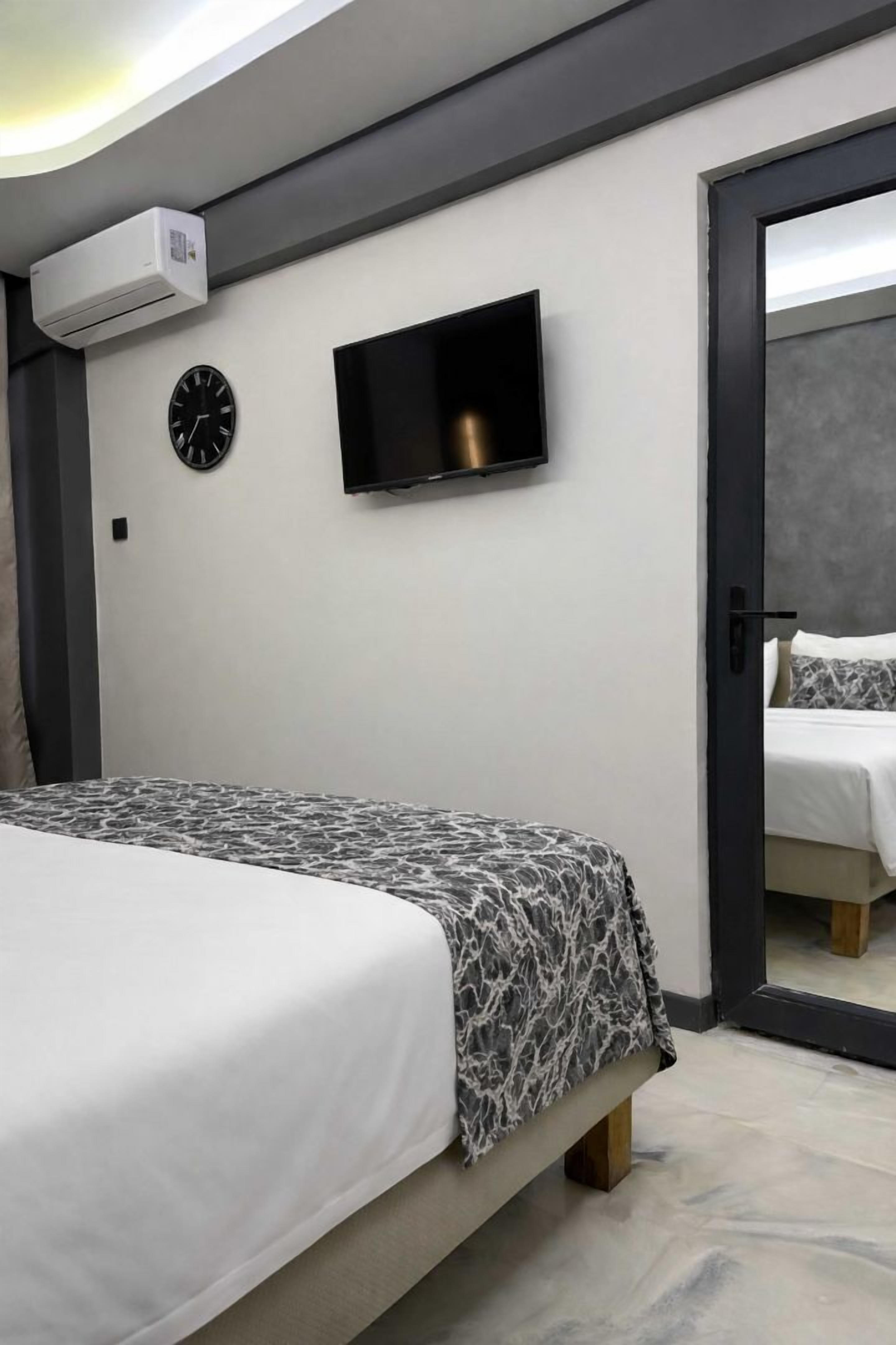 Un dormitorio moderno con una cama, televisor montado en la pared, un reloj y un equipo de aire acondicionado.
