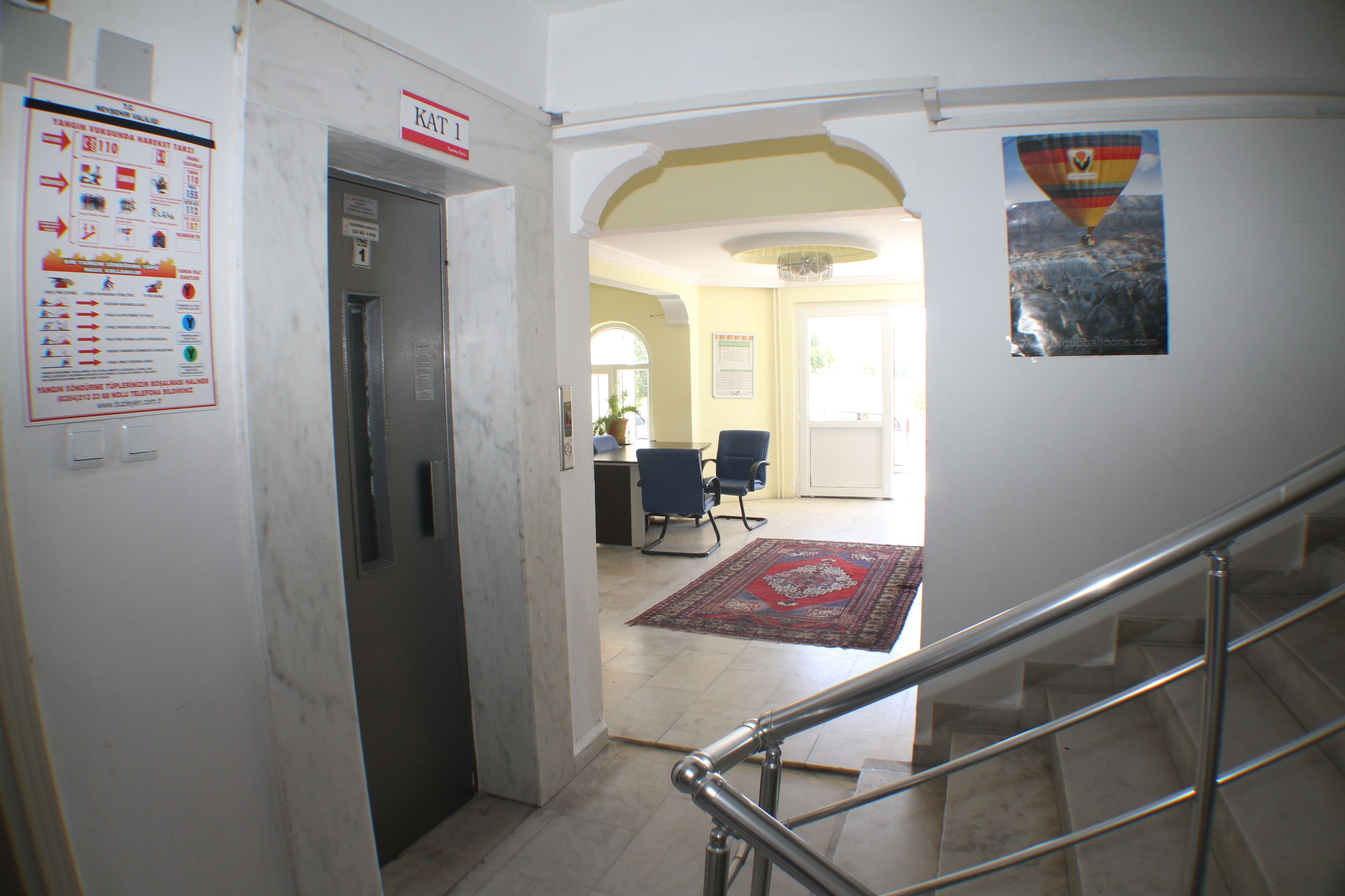 Un vestíbulo de hotel con piso de mármol, una escalera con barandas de metal, un mostrador de recepción y un tapete de diseño rojo.