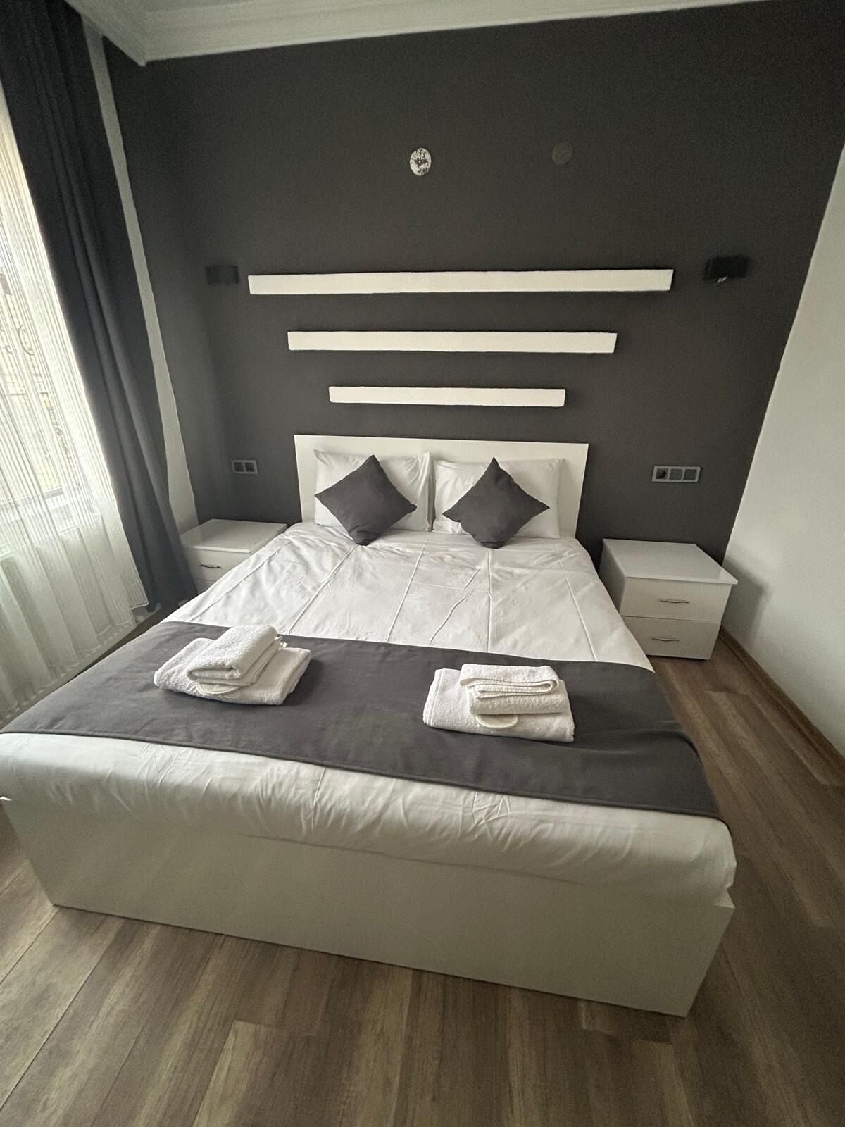 A modern bedroom with a large bed, two bedside tables, and a headboard with built-in lighting.