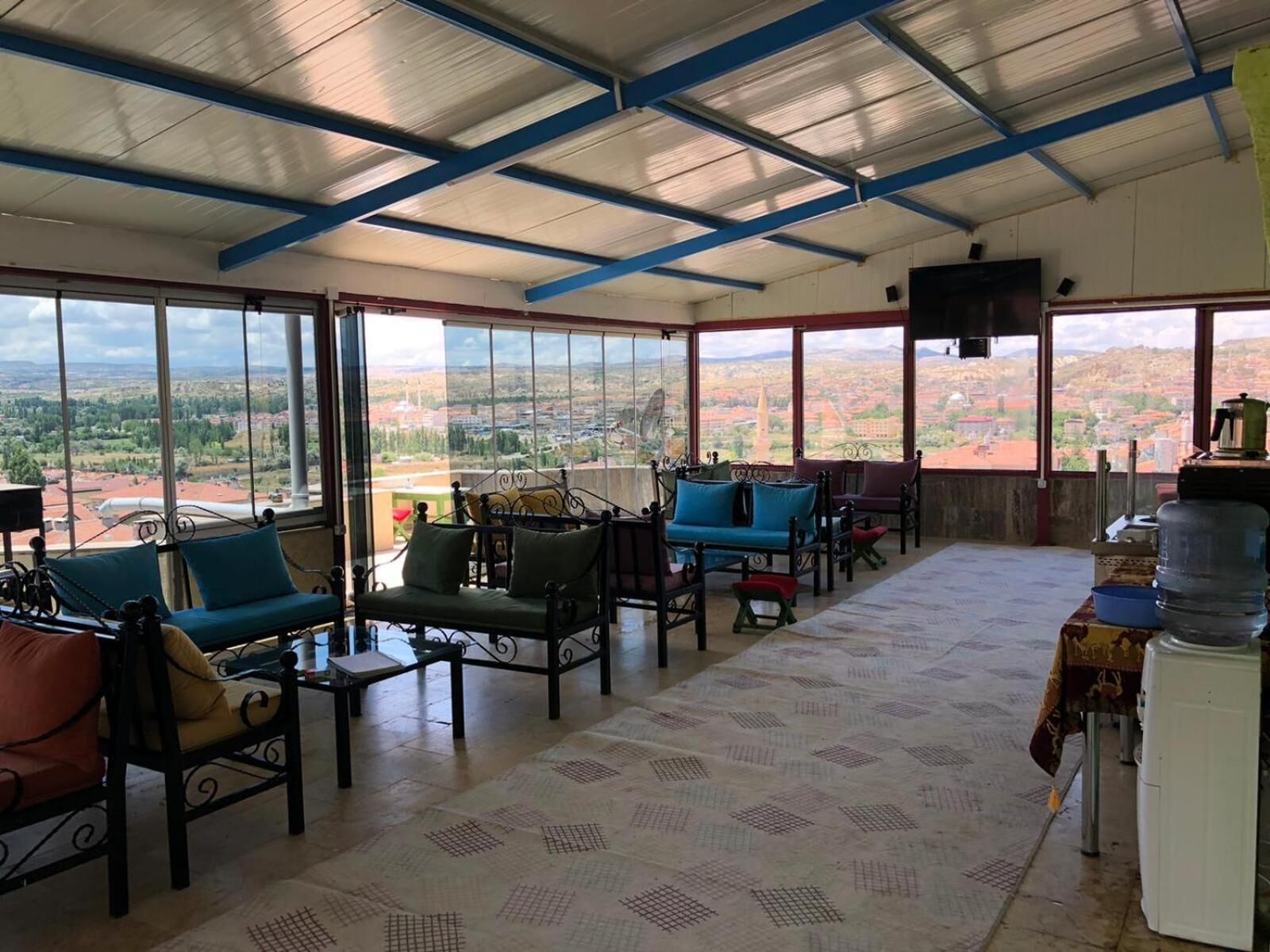 Um quarto espaçoso com teto alto, grandes janelas com vista para a cidade e diversas opções de assentos, incluindo sofás e cadeiras.