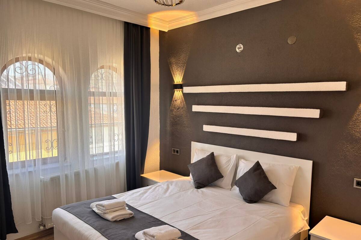 A modern hotel room with a large bed, a bedside table, and a wall-mounted light fixture.