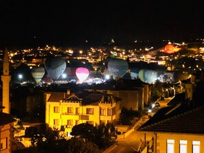 A nighttime view of a town with several buildings and a cluster of hot air balloons in the background. -  Loopy Lodge Hotel (Ürgüp)