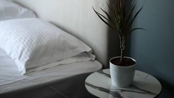 Ein Bett mit weißer Bettwäsche, ein runder Tisch mit einem Blumentopf und eine Wandlampe.
