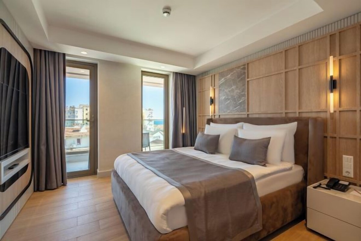 A hotel room with a large bed, a TV, a bedside table, and a view of the city.