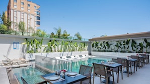 A rooftop pool area with lounge chairs, dining tables, and a view of a high-rise building. - Awen Lara Hotel (Antalya)