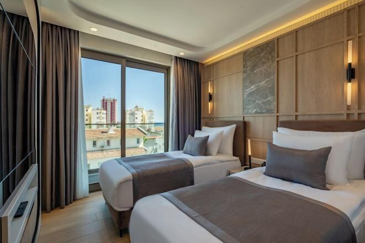 A hotel room with two beds, a large window, and a city view.