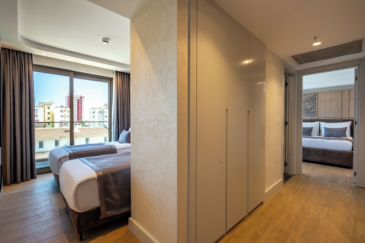 A hotel room with a balcony, a large bed, a wardrobe, and a view of the cityscape.