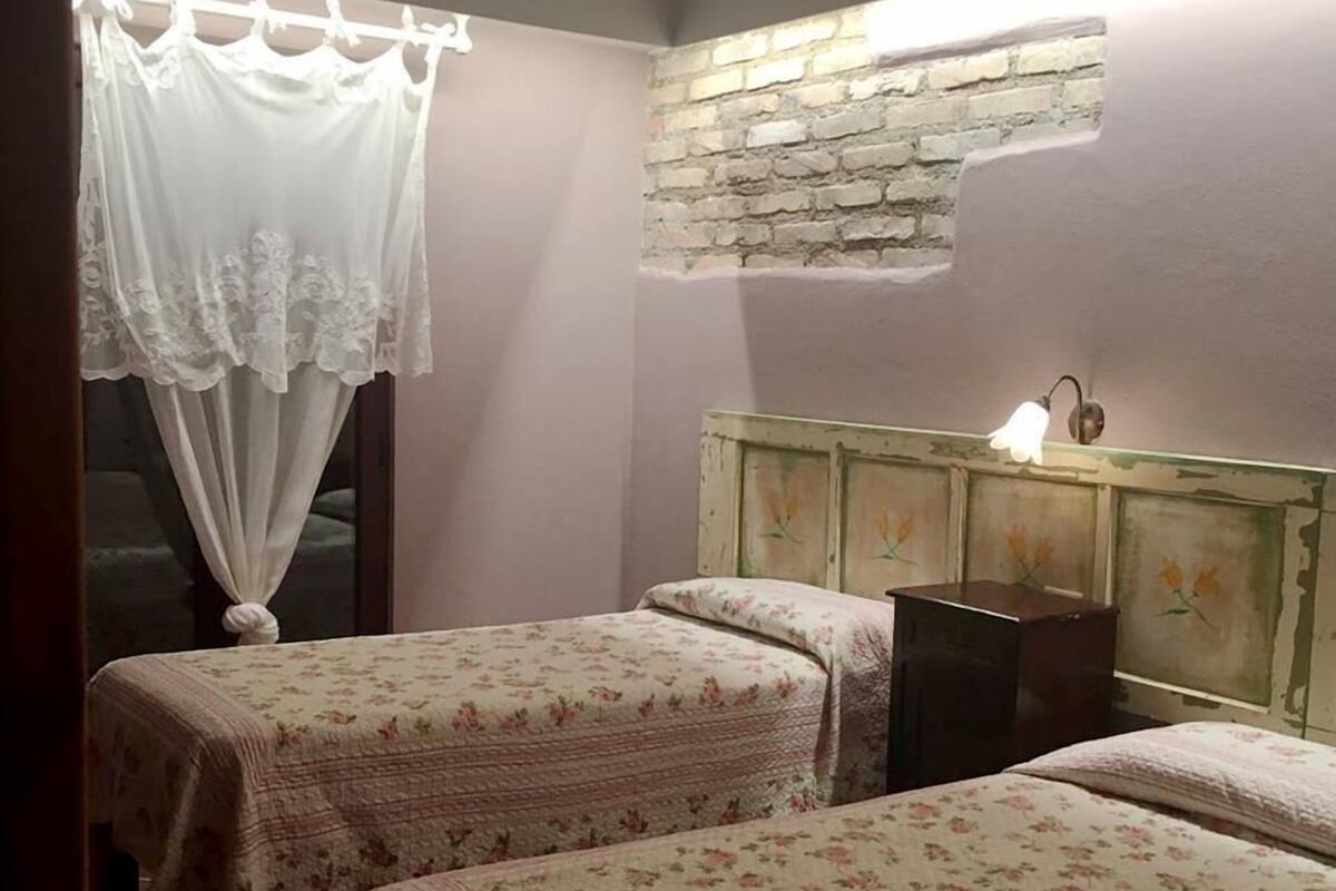Quarto com duas camas, uma parede de pedra e um armário de madeira iluminado.