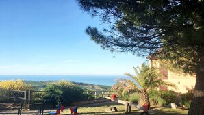 Um parquinho com balanços e escorrega, cercado por árvores e com vista para o oceano.
