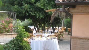 Un'area pranzo all'aperto con tavoli rotondi ricoperti da tovaglie bianche, circondata da vegetazione e alberi.