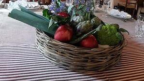 Uma área de refeições com teto de madeira rústica, um mural na parede com pássaros e uma mesa de buffet com arranjo central de legumes e flores.