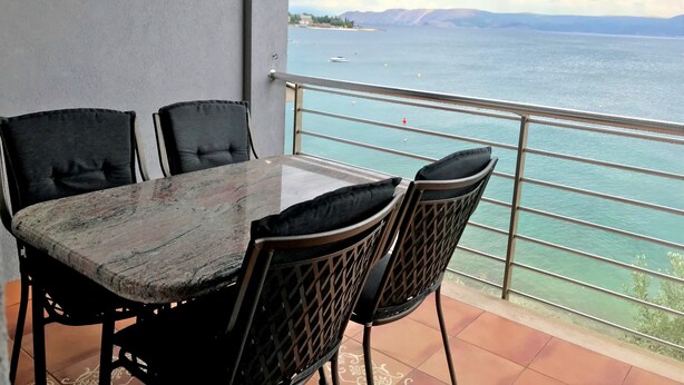 A balcony with a table and chairs, overlooking a body of water and distant mountains. - Apartmani Alagic (Crikvenica)
