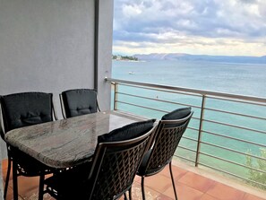 A balcony with a table and chairs, overlooking a body of water and distant mountains.