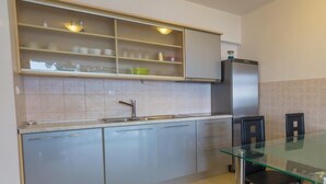 A modern kitchen with a glass dining table, stainless steel appliances, and light-colored cabinets. - Apartmani Alagic (Crikvenica)