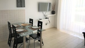 A modern dining area with a glass table, black chairs, and a mounted TV. - Apartmani Alagic (Crikvenica)