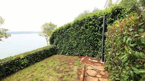 A landscaped garden with a stone pathway leading to a seating area, surrounded by lush greenery and overlooking a body of water. - Apartmani Alagic (Crikvenica)