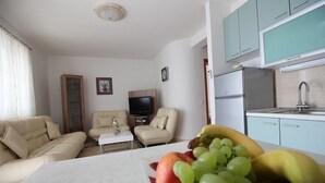 A living room with a sofa, a coffee table, and a TV. There is a kitchen with a sink and cabinets. - Apartmani Alagic (Crikvenica)