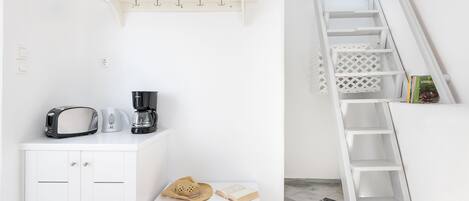 Uma cozinha clara com torradeira, máquina de café e um chapéu sobre uma pequena mesa.