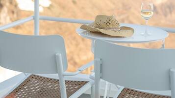 Mesa de metal blanco con una copa de vino blanco y un sombrero de paja, con montañas al fondo.