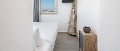 A hotel room with a bed, a TV mounted on the wall, a window with a view, and a wooden shelf with a bowl.