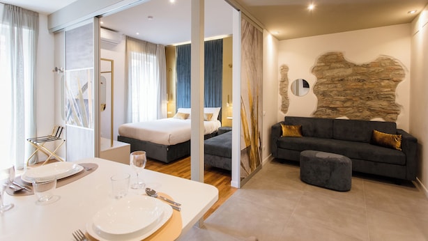 Moderni hotellihuone, jossa on ruokailutila, sänky, sohva ja kivestä tehty koristeellinen seinä.