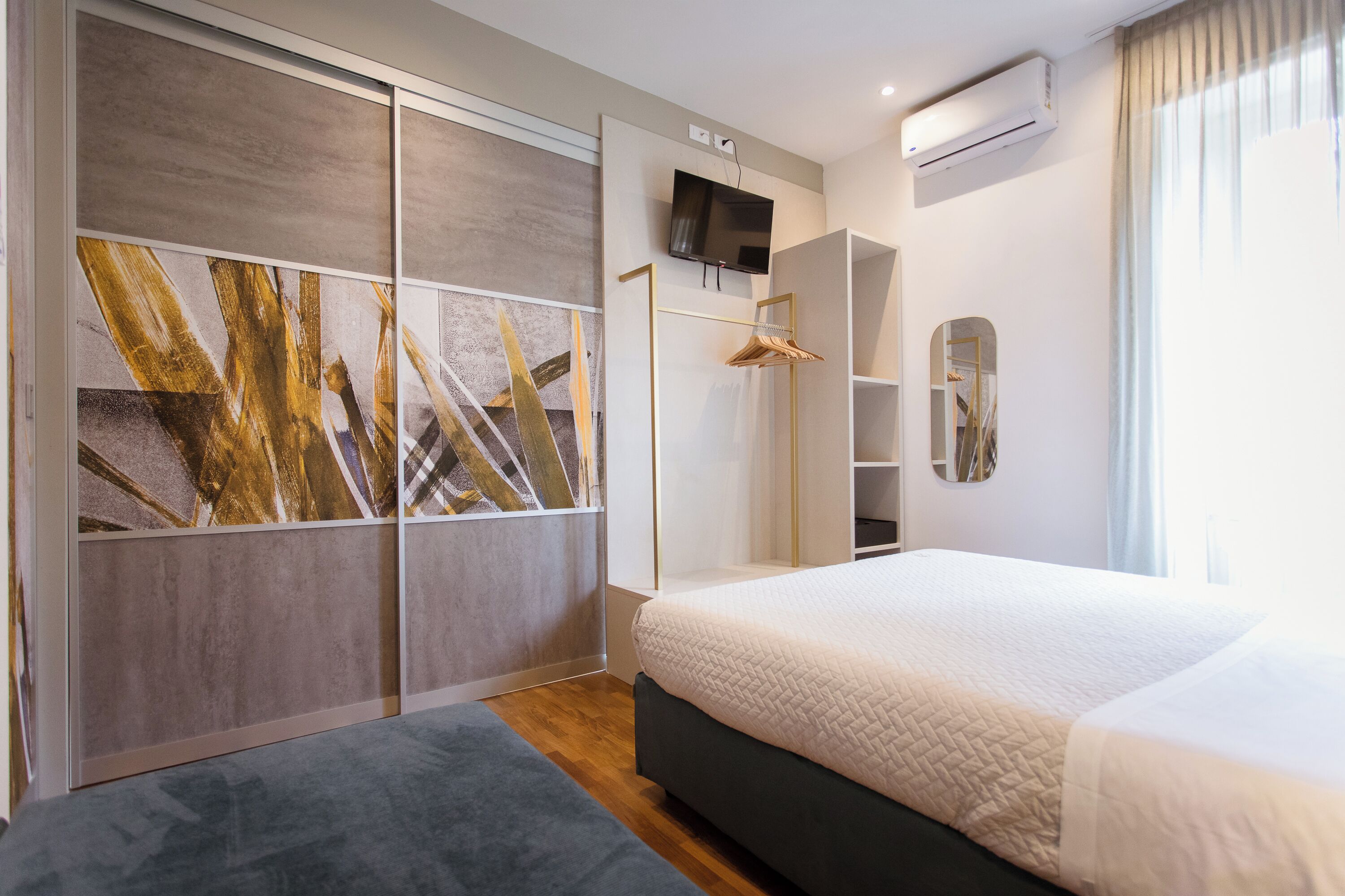 A modern bedroom with a large bed, a wardrobe with a mirror, and a TV mounted on the wall.