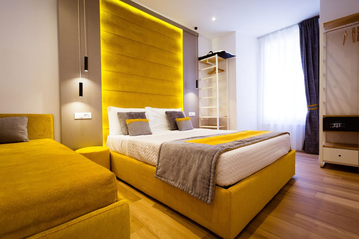 Ein modernes Hotelzimmer mit einem großen Bett, Nachttischen, einem Kleiderschrank und einer eingebauten Ablagefläche.