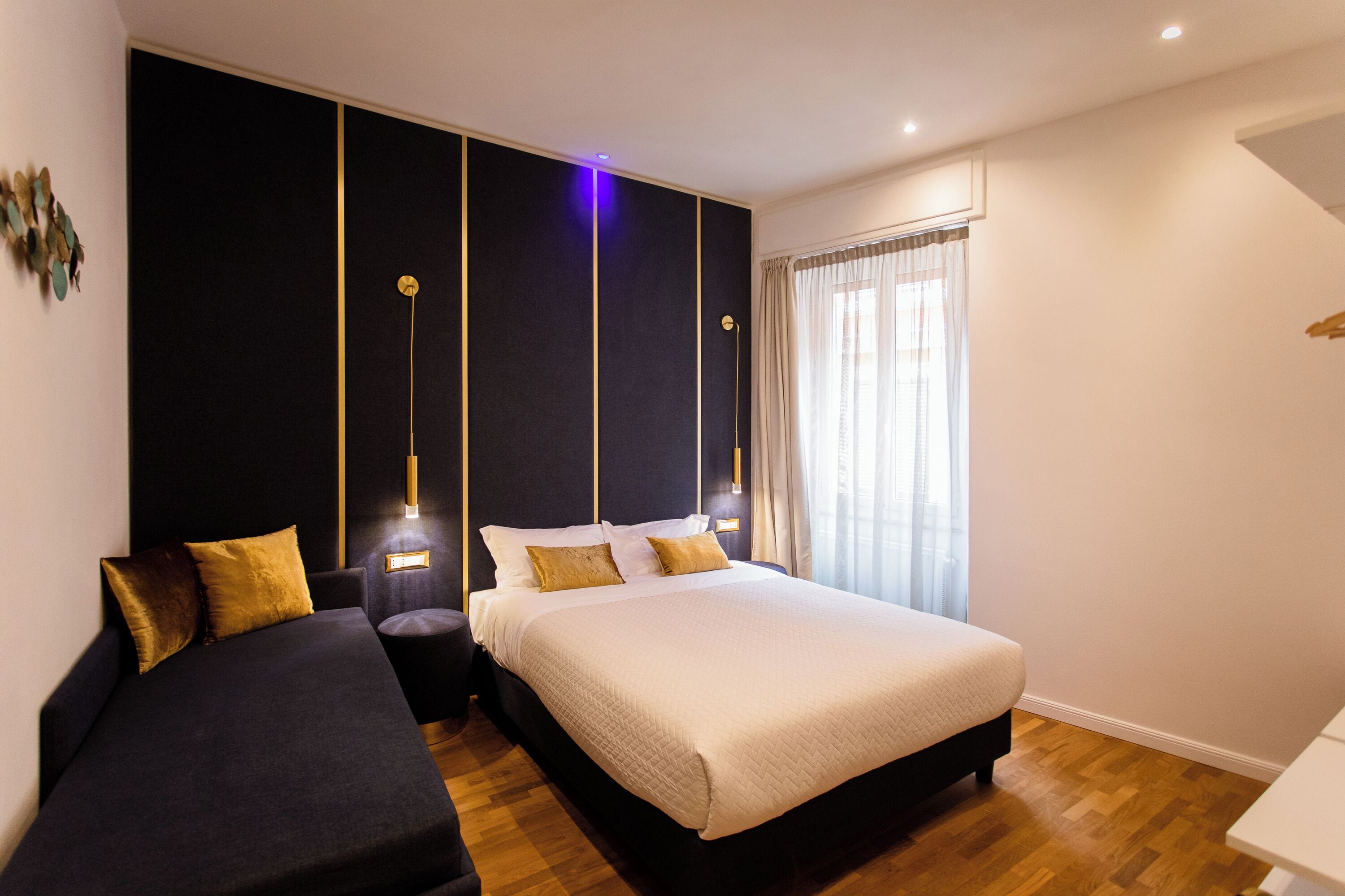 Een moderne slaapkamer met een groot bed, een kleinere bank en een nachtkastje met een lamp.