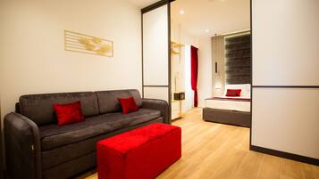 Un salon moderne avec un canapé gris, des coussins rouges et un pouf rouge. Un grand miroir reflète la pièce, et on peut voir un plancher en bois.