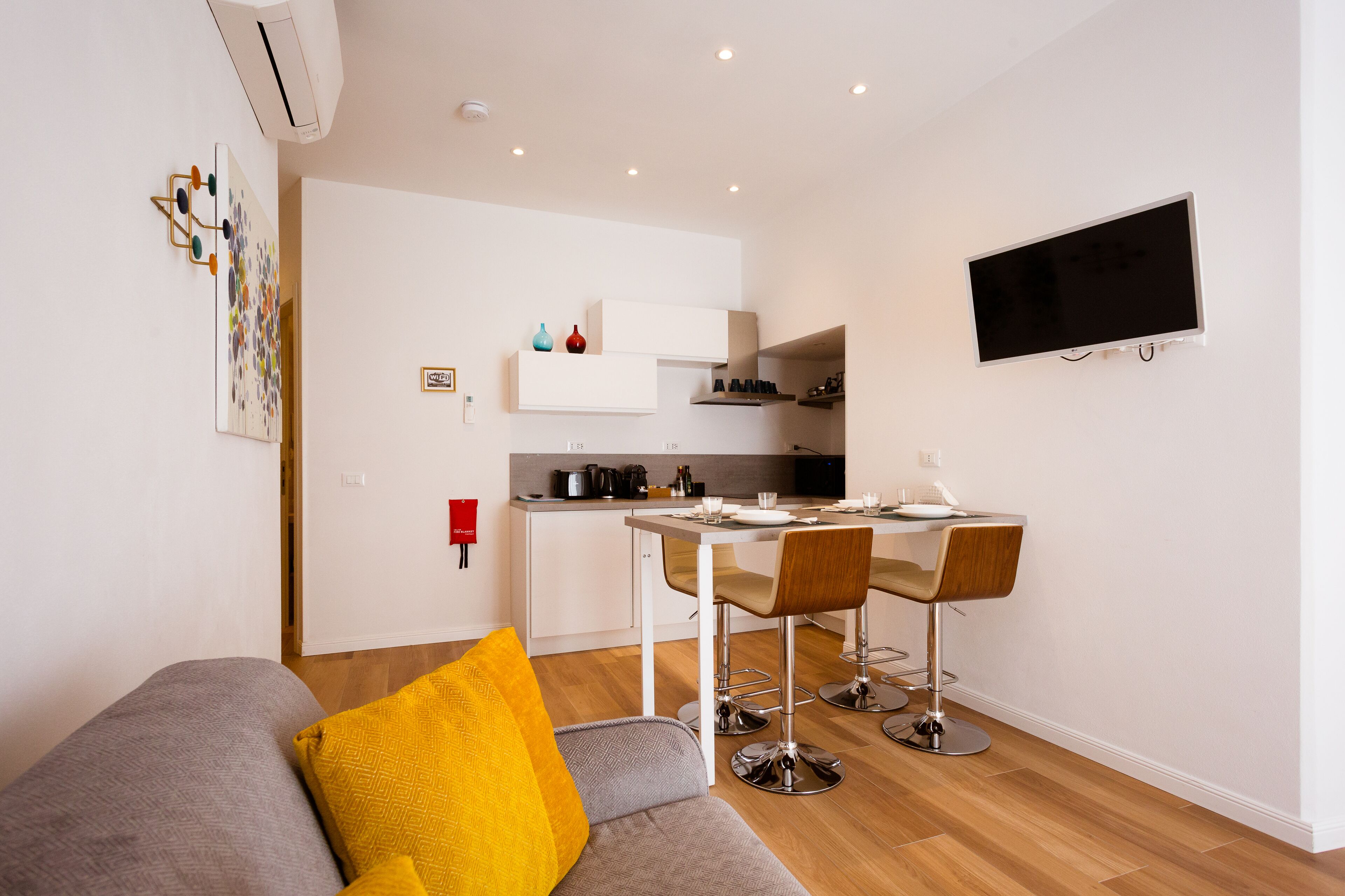 A modern apartment with a dining area, kitchenette, and a living room with a sofa and a TV.