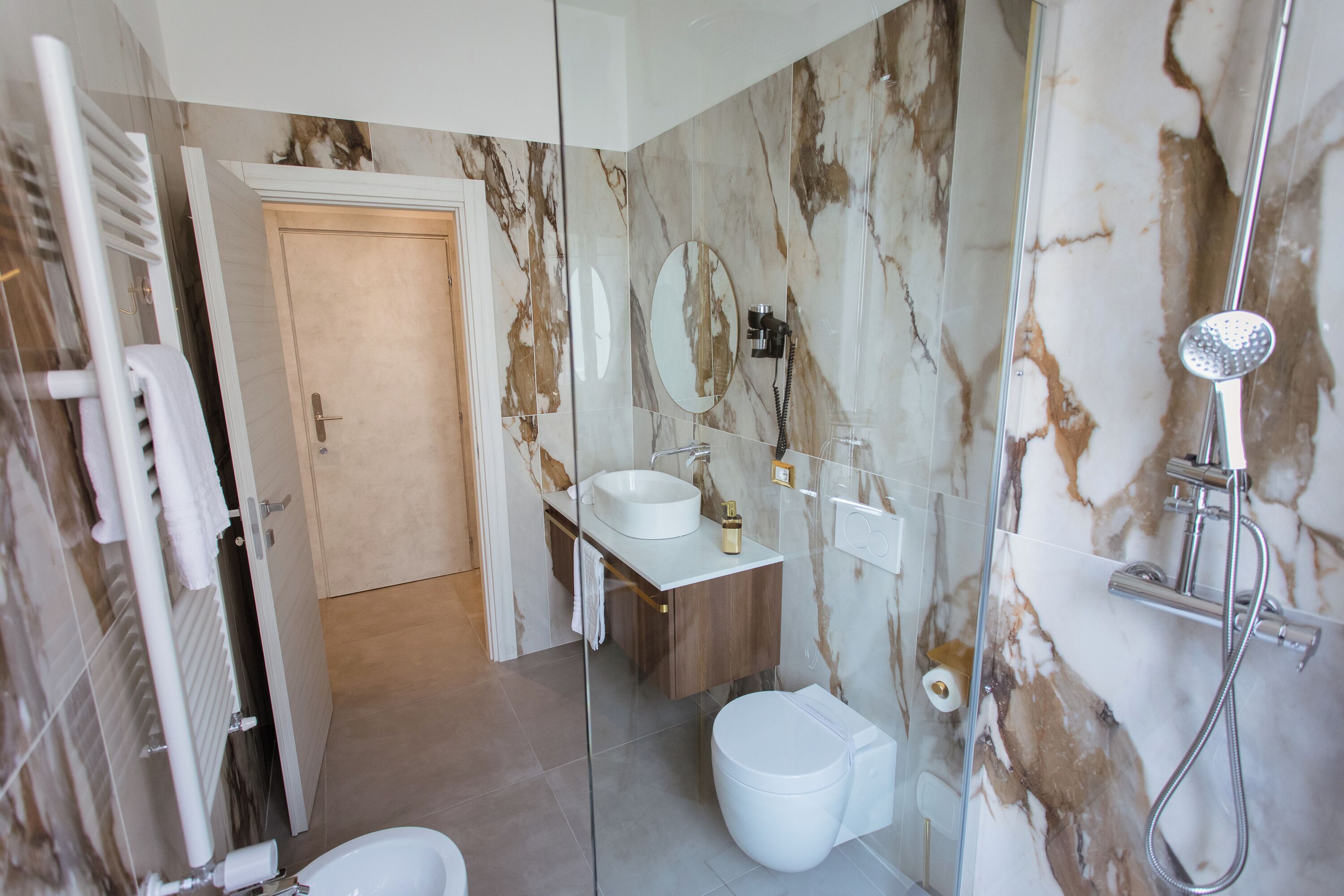 Un baño moderno con ducha envuelta en vidrio, lavamanos blanco y salpicadero de mármol.