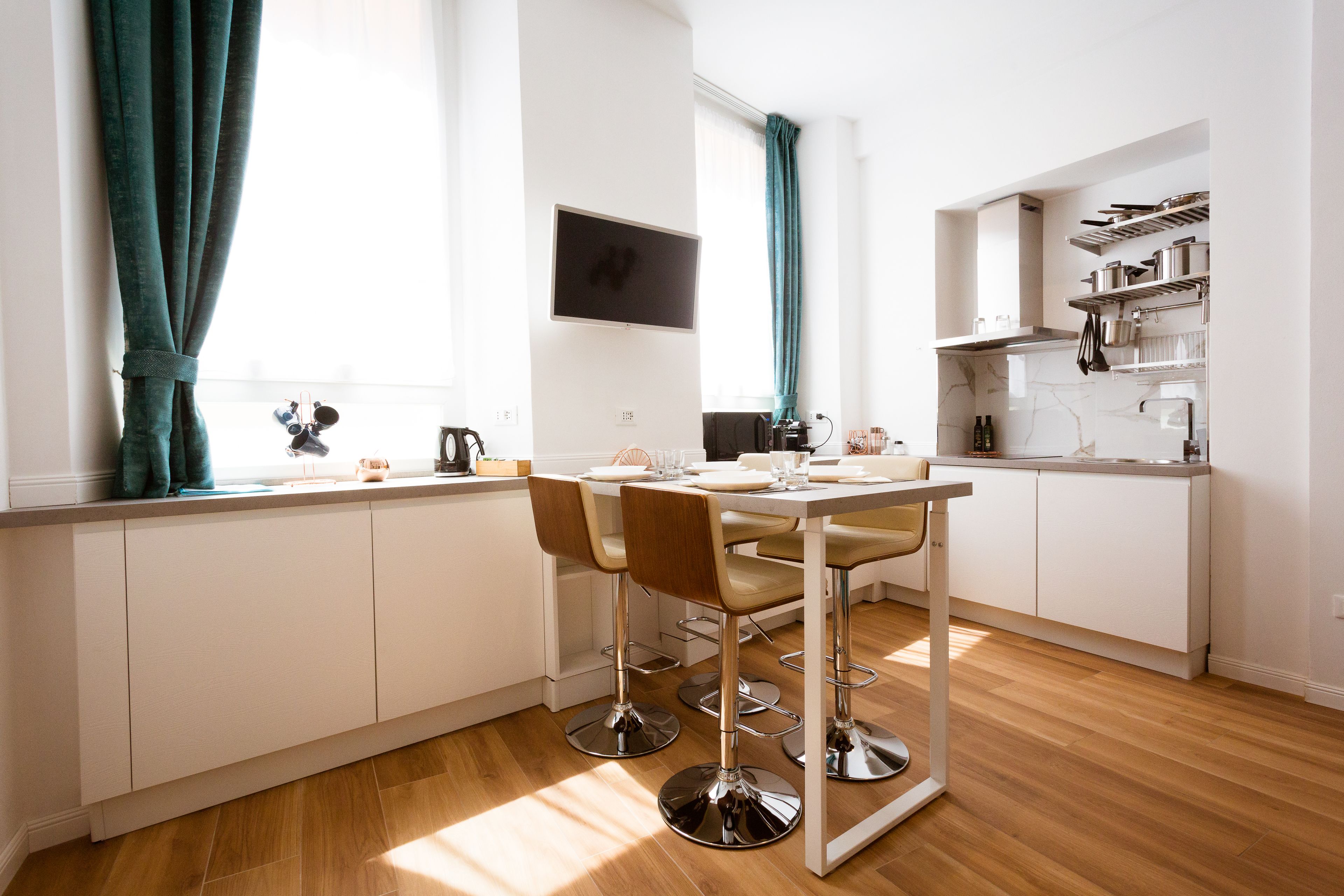 Une cuisine moderne avec des meubles blancs, un plan de travail en acier inoxydable et un coin repas comprenant une table et des chaises.