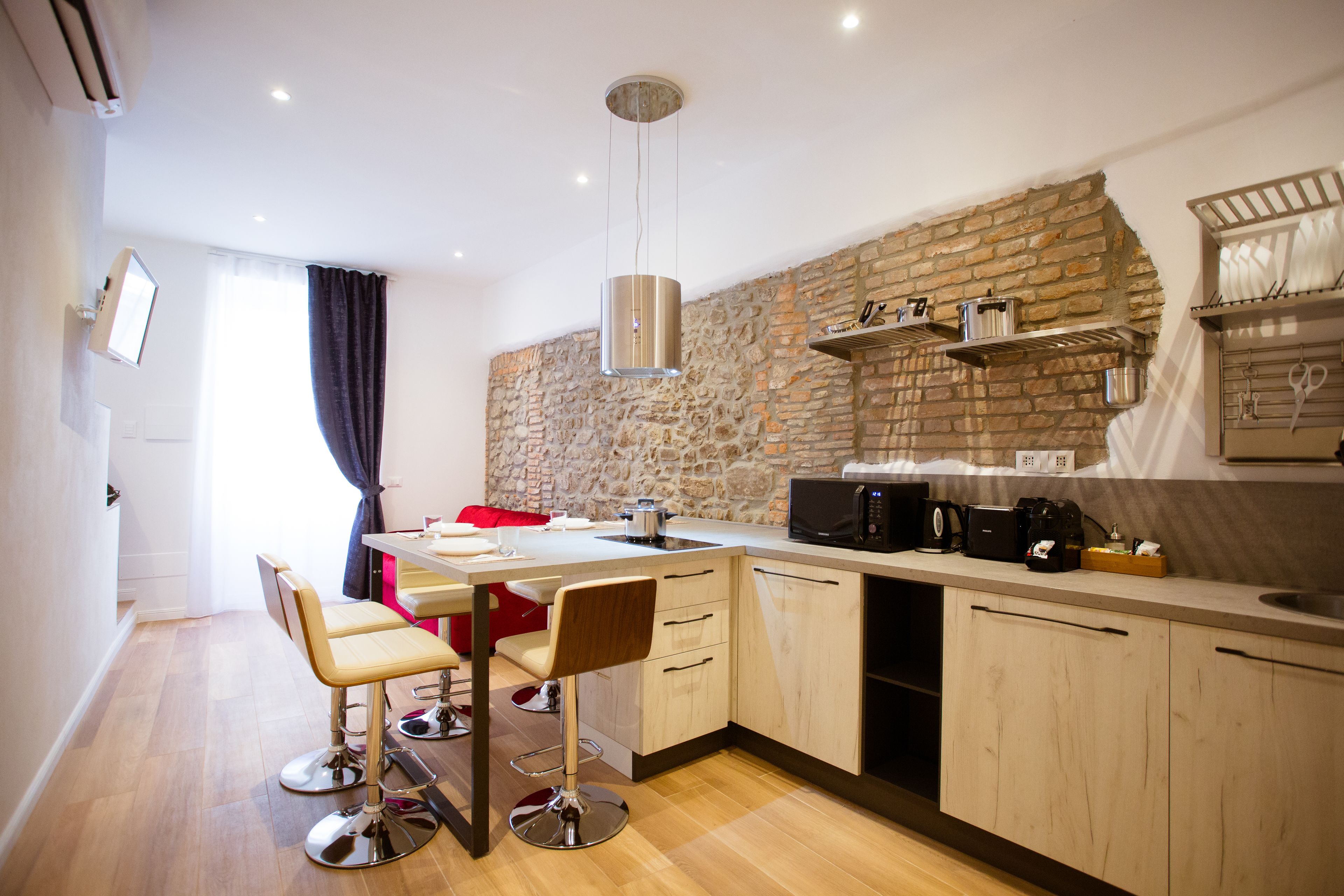 A modern kitchen with a stone wall, wooden cabinets, a dining area with two chairs, and a hanging light fixture.