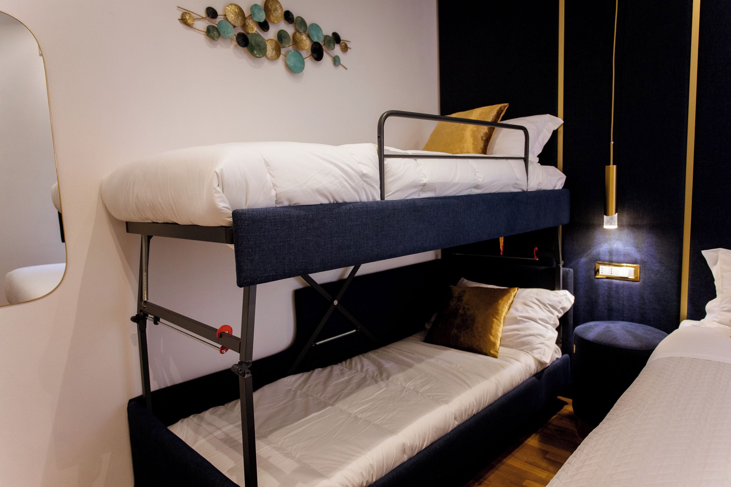 Una cama litera con cabecera, una mesita de noche y un aplique de pared.