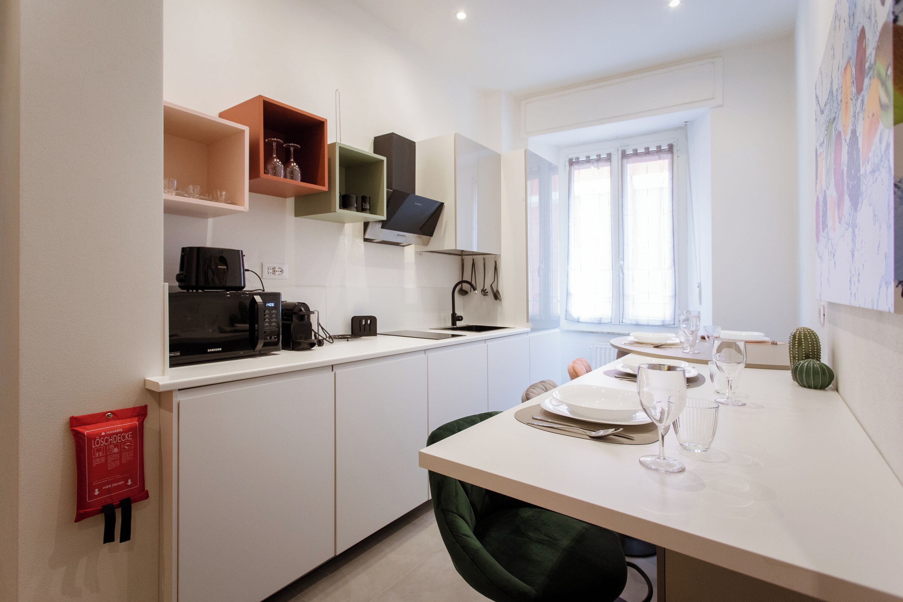 Una cocina moderna con armarios blancos, microondas, cafetera y un comedor con una mesa dispuesta para dos.