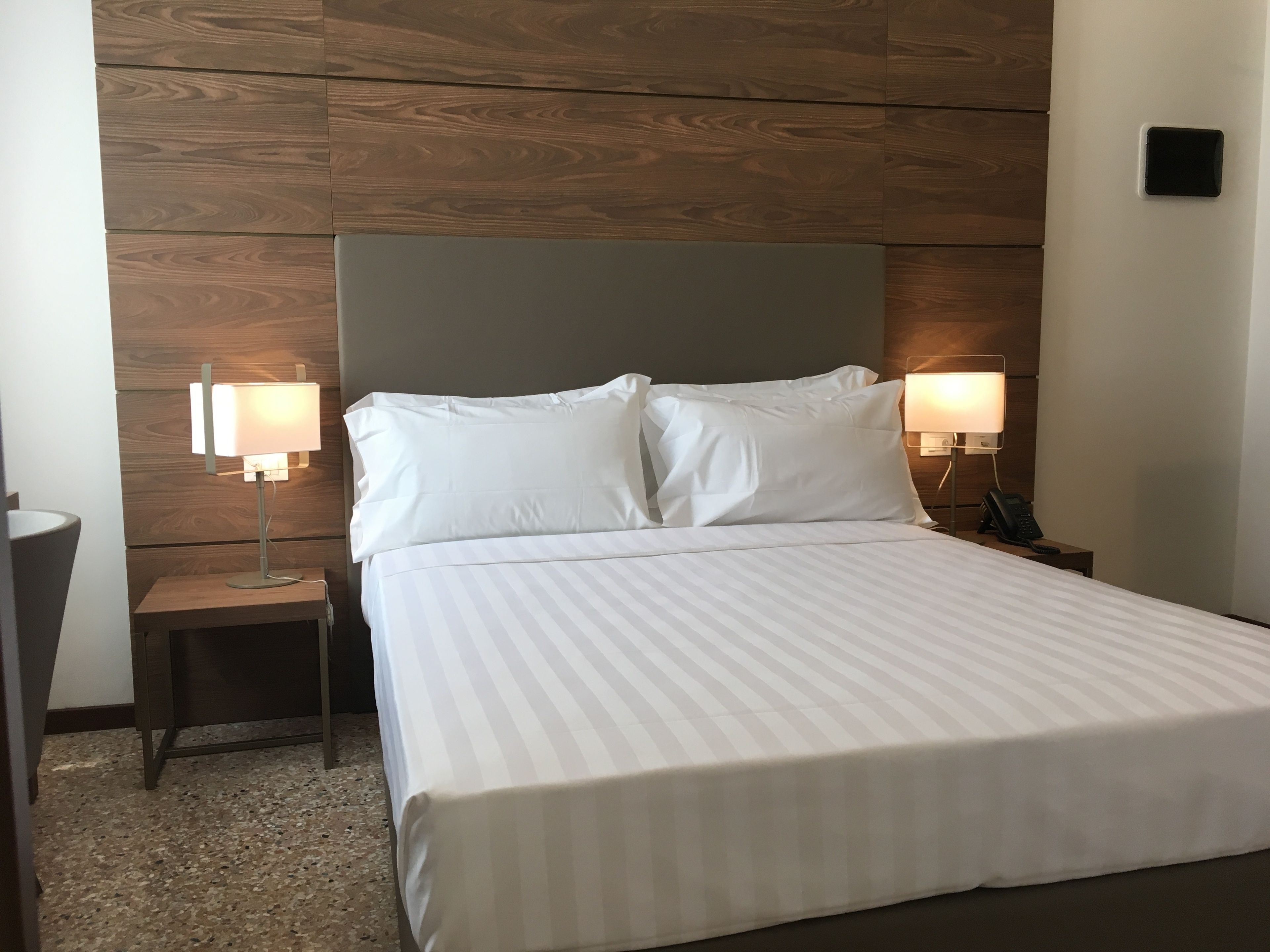 A hotel room with a large bed, two bedside tables with lamps, and a wooden wall paneling.