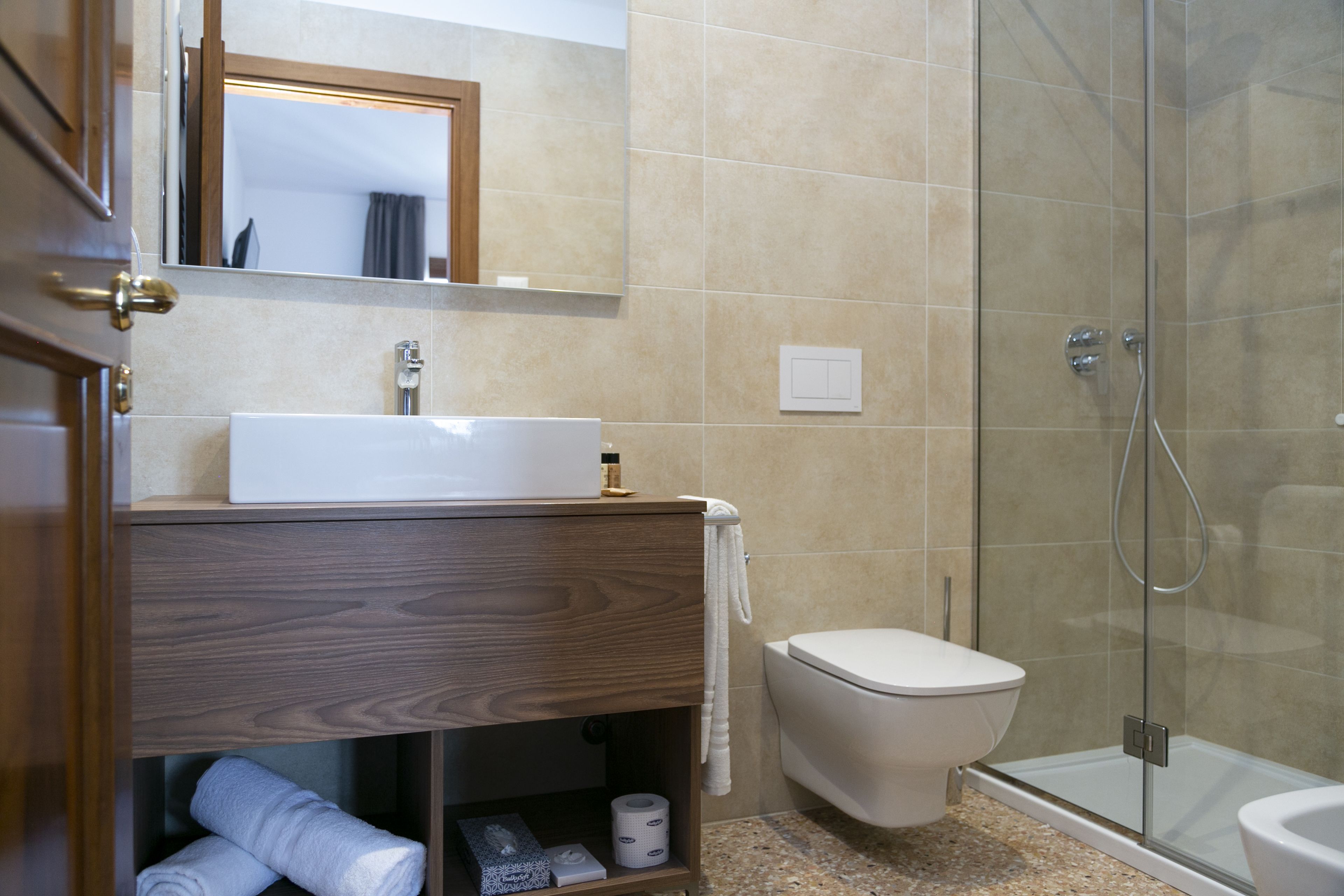 A modern bathroom with a wooden vanity, a white sink, a toilet, and a glass-enclosed shower.