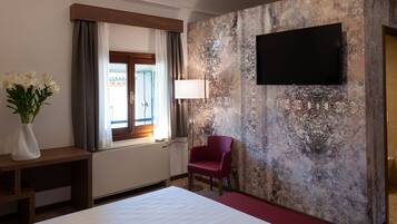 Een hotelkamer met een bed, een bureau, een stoel, een aan de muur bevestigde televisie en een raam met gordijnen.