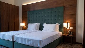 A double bed with a green upholstered headboard, two bedside lamps, and a small bedside table with a phone and charger.
