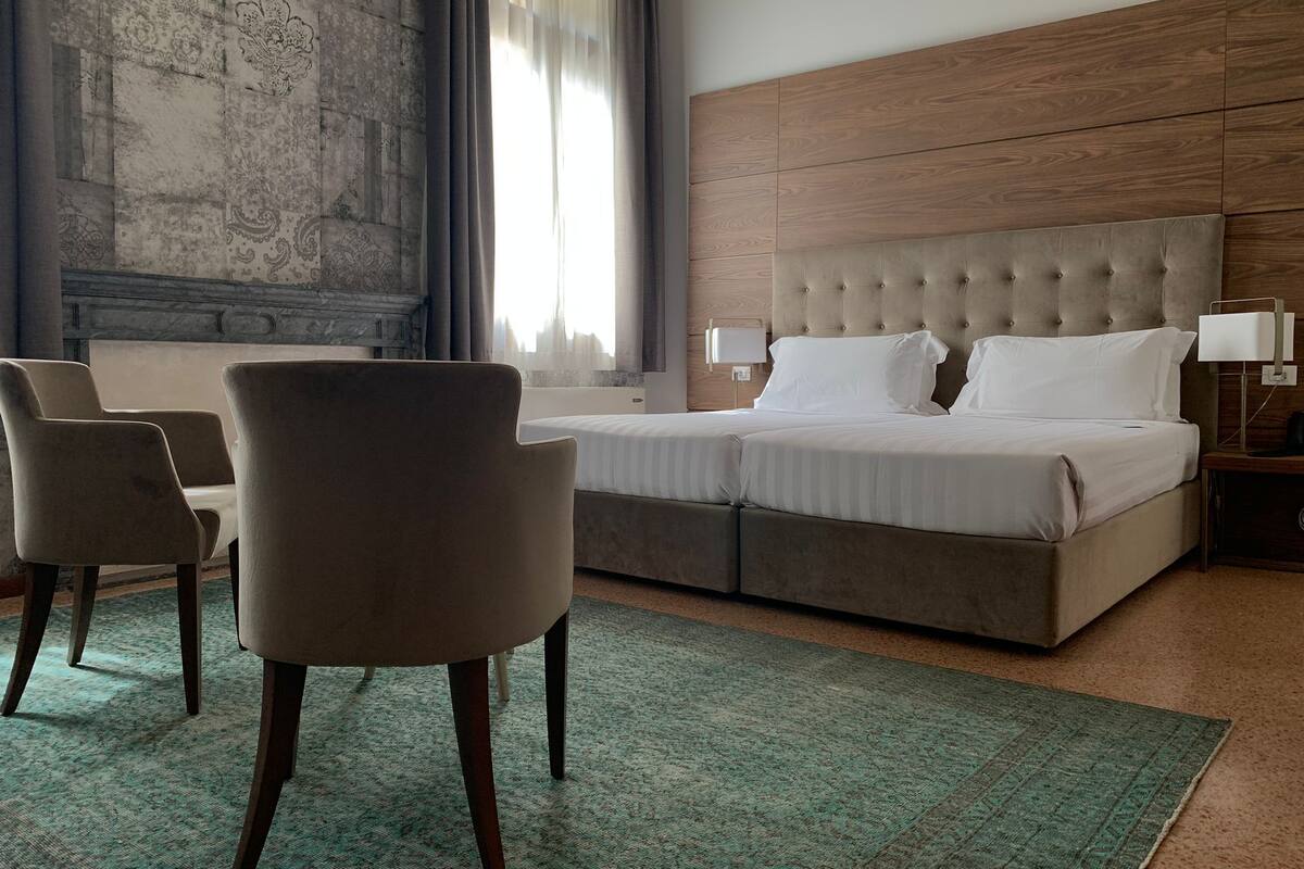 A hotel room with a large bed, two armchairs, a nightstand, and a large window with curtains.