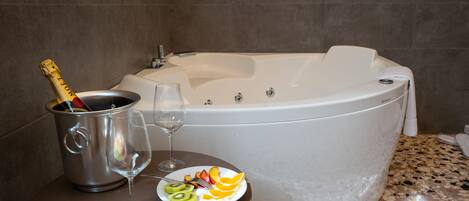 A spa area with a large bathtub, a fruit plate, a champagne bottle, and two glasses on a table.