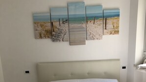 Een slaapkamer met een bed, een klein nachtkastje en een wanddecoratie met een strandgezicht.