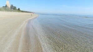 Een strand met helder water, een zandstrand en een torenachtige constructie op de achtergrond.