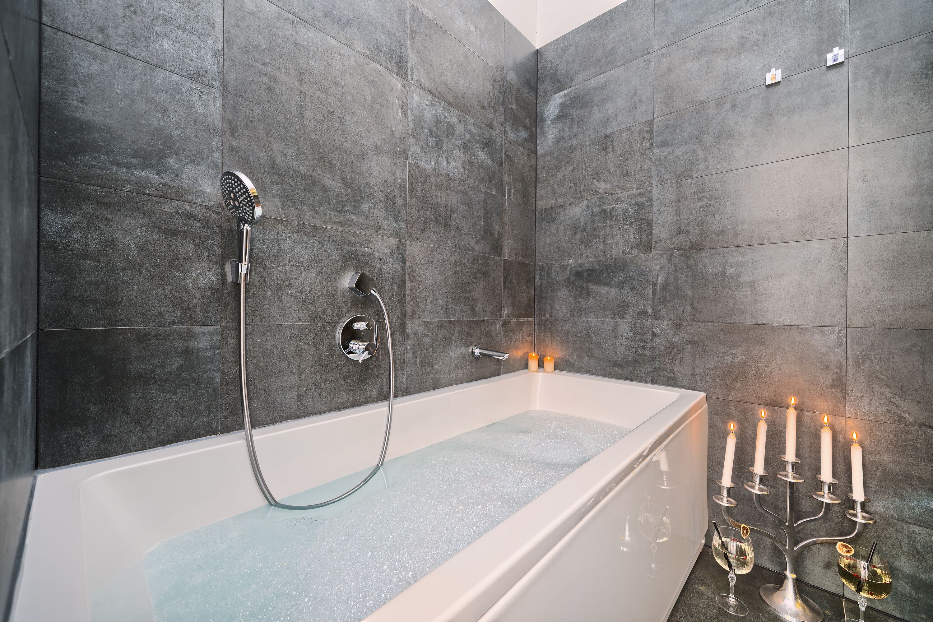 Une salle de bain moderne avec une baignoire sur pieds, une douchette et un porte-bougies avec des bougies allumées.