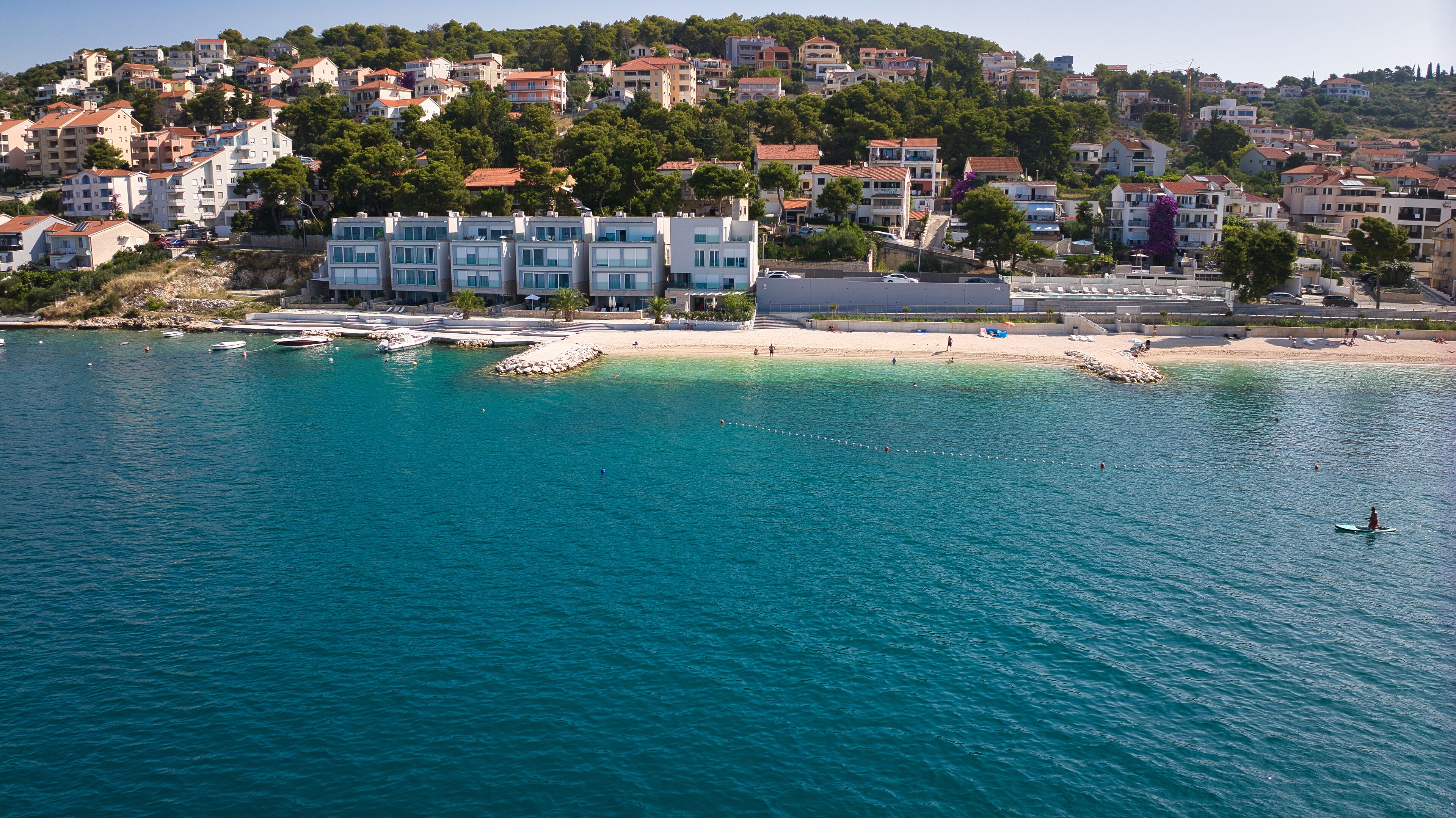 Une ville côtière avec des bâtiments qui bordent la plage, une étendue de sable et une eau d’un bleu limpide.