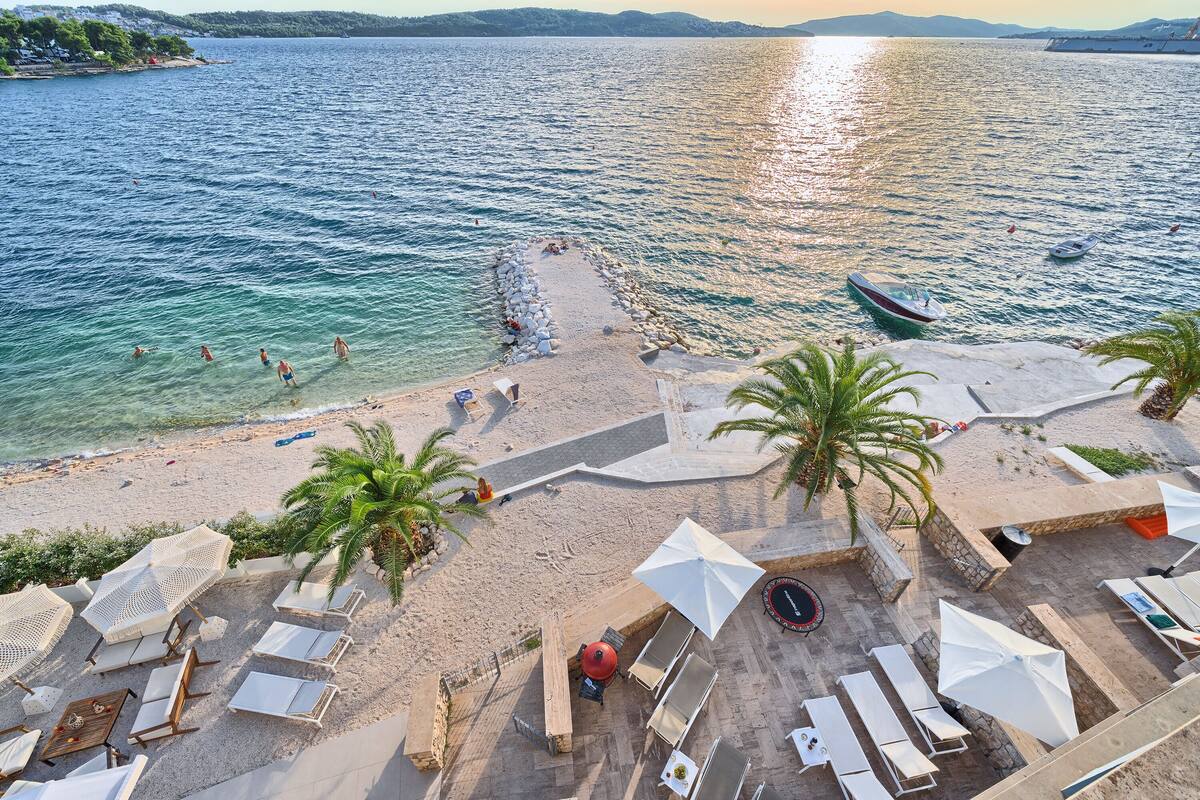 A beach with clear waters, sun loungers, umbrellas, and a boat.