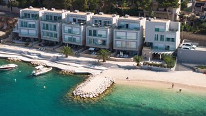 Un hotel sul lungomare con numerosi balconi, una spiaggia sabbiosa e un porto turistico con barche.