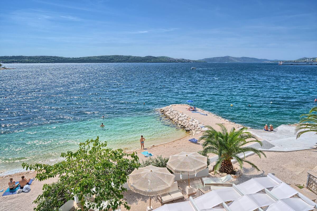 A beach with clear waters, umbrellas, and lounge chairs.