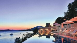 Una piscina a sfioro tranquilla con vista chiara sul mare e sulle barche, circondata da sdraio e ombrelloni.