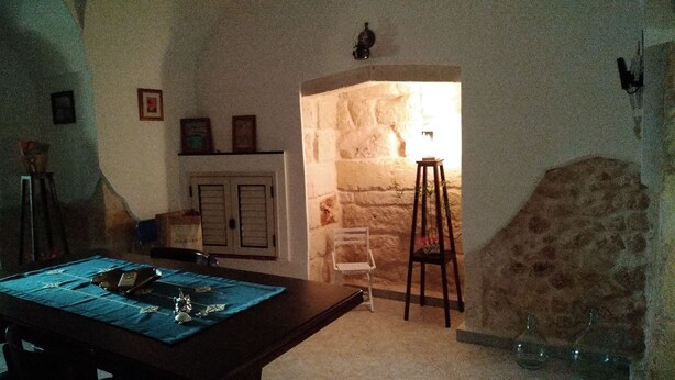 Une pièce avec un mur en pierre, une table en bois recouverte d’une nappe bleue, une chaise blanche et un petit tabouret.